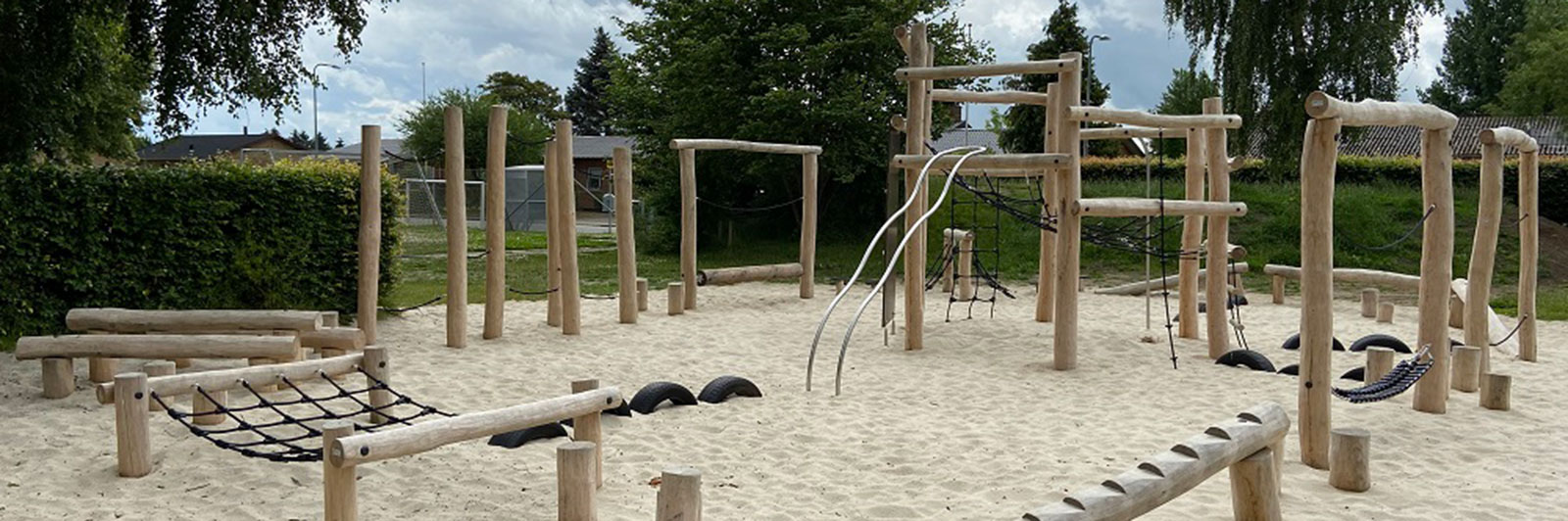 A large, natural wood obstacle course at a playground with sand floor.